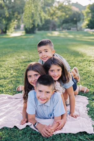 A group lies together on a pink blanket in the grass during an outdoor photo session.