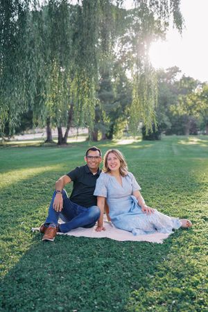 Couple relaxing on blanket during outdoor photo session under willow trees.