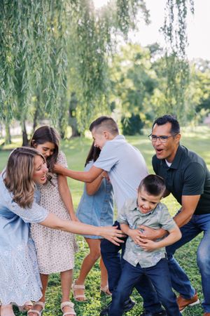 A playful family photoshoot sequence showing candid laughter and interaction under a weeping willow tree in a park.