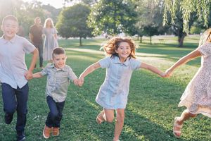 People jumping and playing together joyfully on grass under willow trees in a park setting.