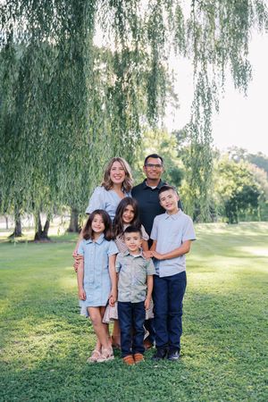 Family portrait session under a weeping willow tree in a sunny park setting.