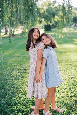 Two children playing and laughing together on green grass under willow trees.