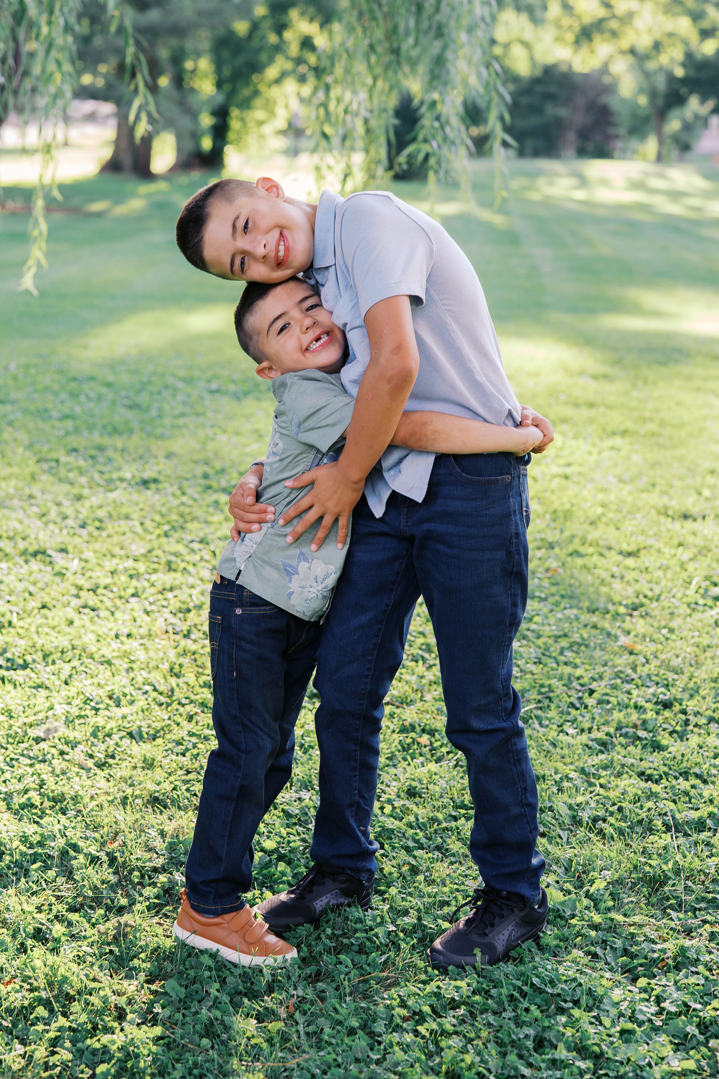 Two children playfully wrestle and hug on green grass in casual clothing.