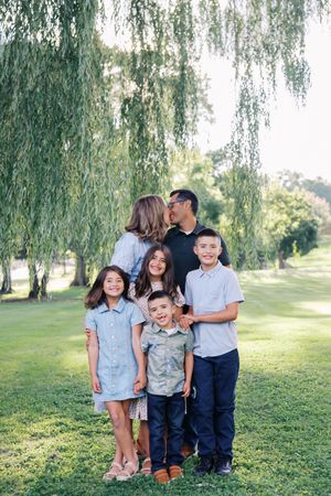 A playful family photo session under a weeping willow tree on a sunny day.