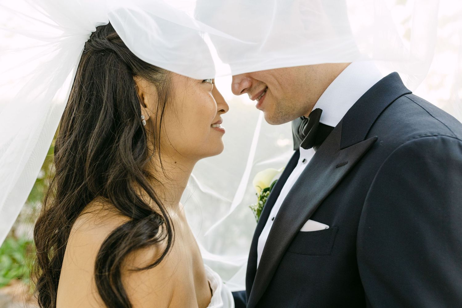Close up portrait of bride and groom under veil sharing intimate moment in soft natural light