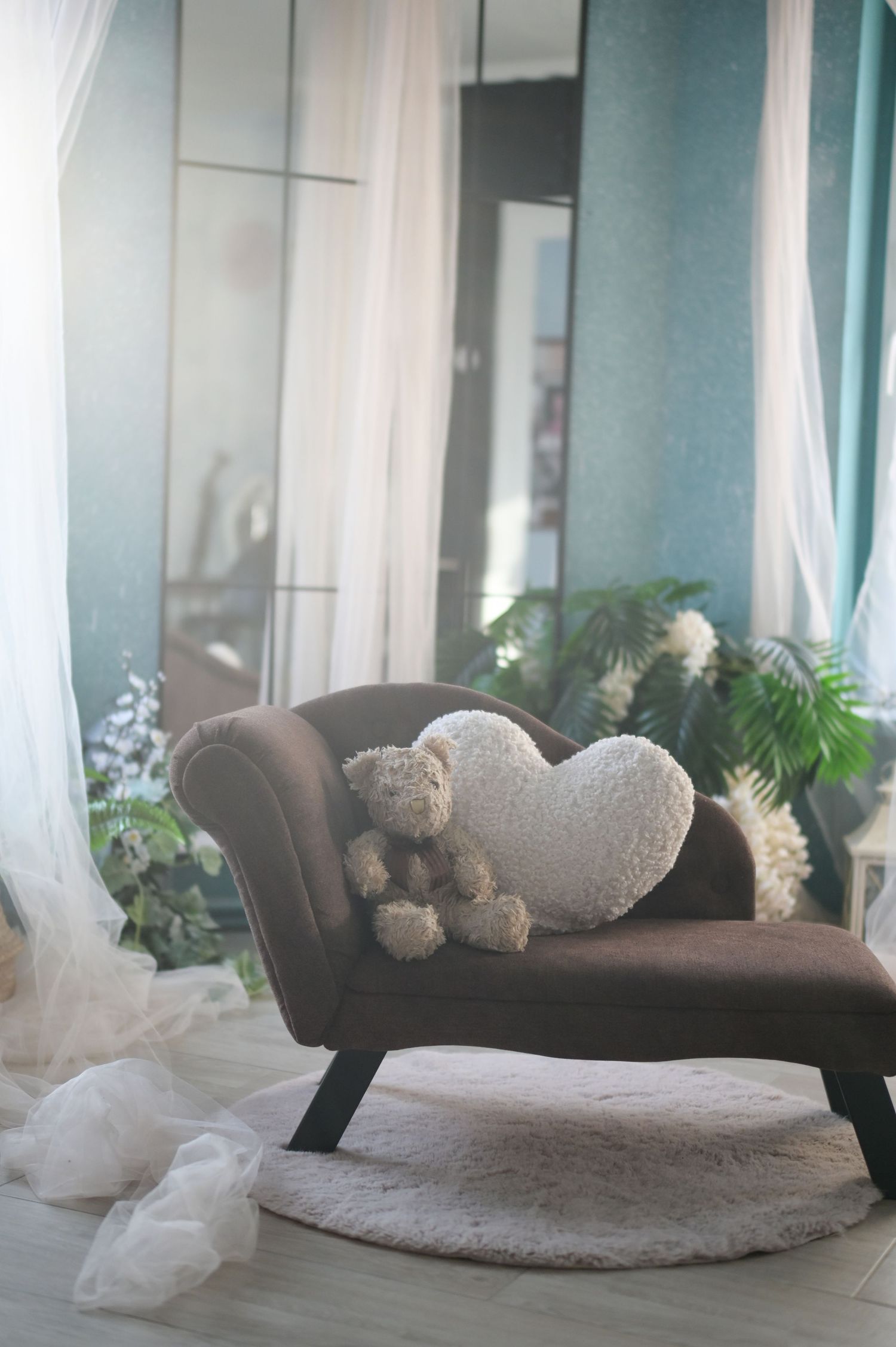 A brown couch with decorative pillows and sheer white curtains in a bright, modern living room setting.