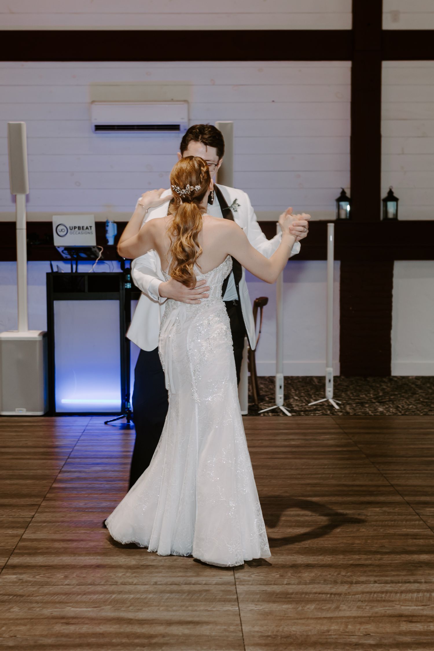 Bride and groom share intimate first dance embracing on wooden dance floor at elegant wedding reception.