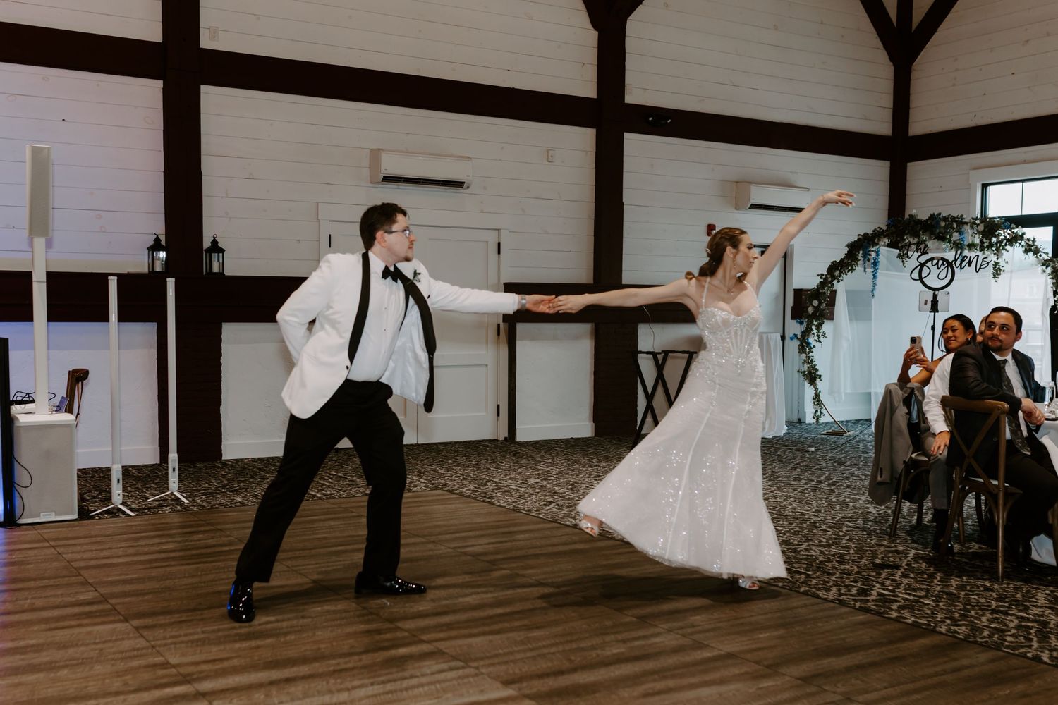 Bride and groom perform energetic choreographed first dance in white barn wedding reception venue.