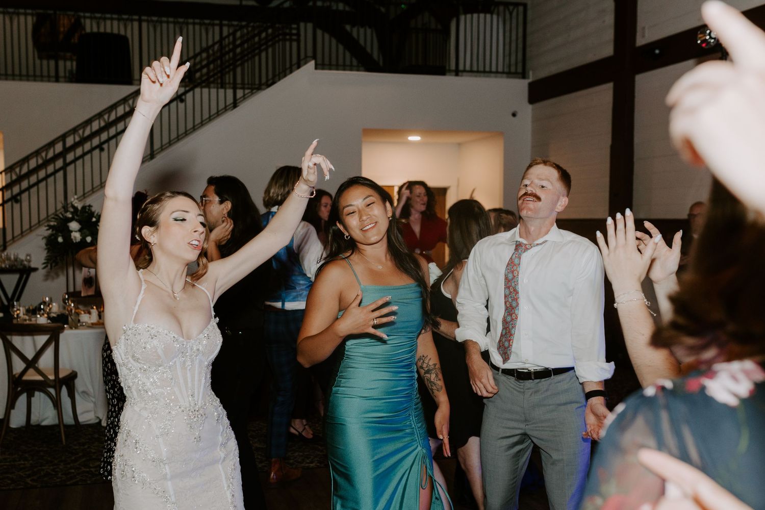 Bride and bridesmaid in teal dress dance joyfully with guests at lively wedding reception.