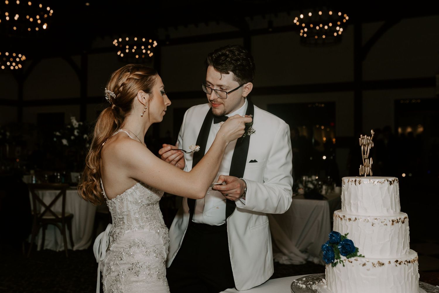 Bride feeds groom wedding cake as they celebrate beside their elegant three-tier white cake.