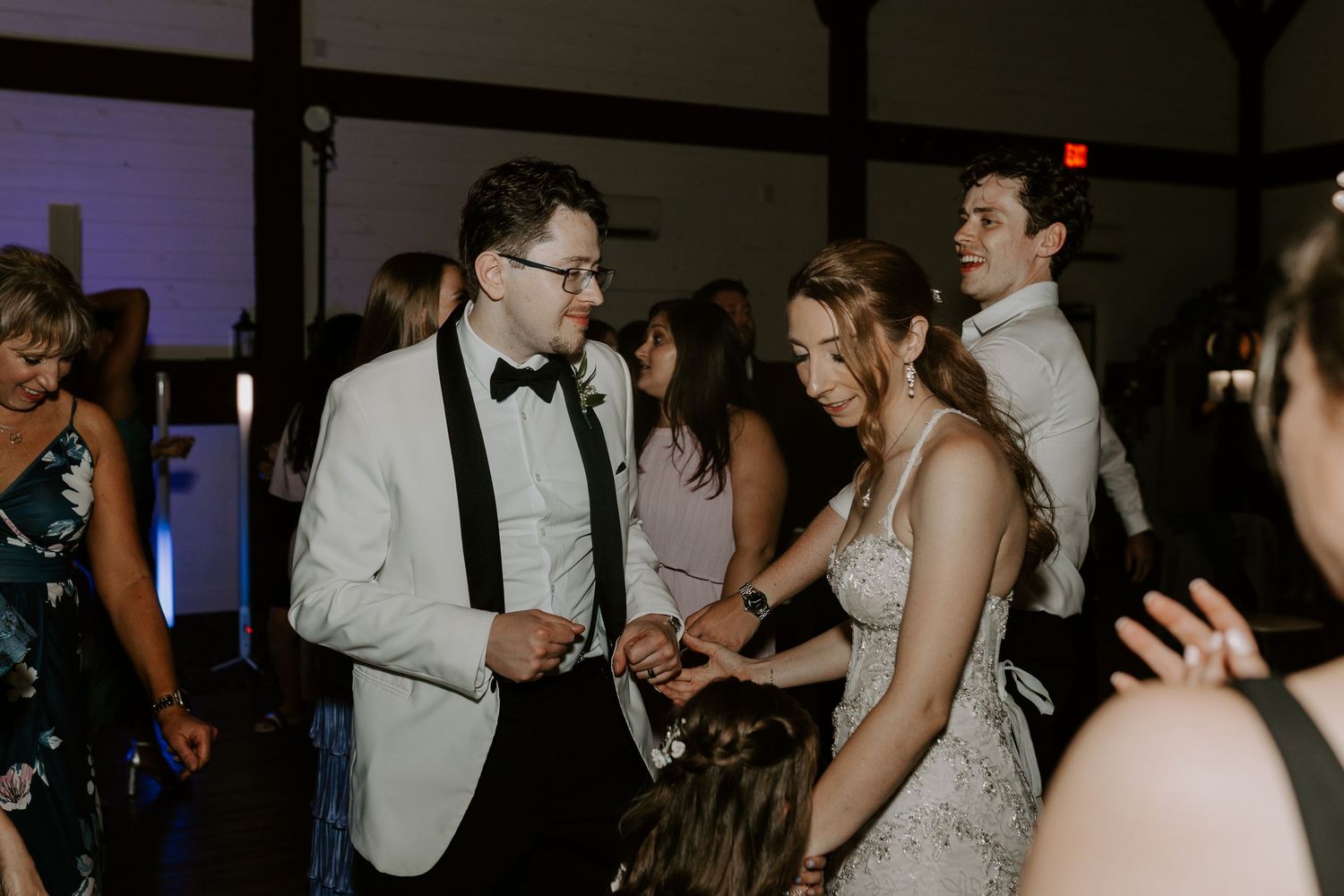 Bride and groom dance and laugh together with guests at their wedding reception.
