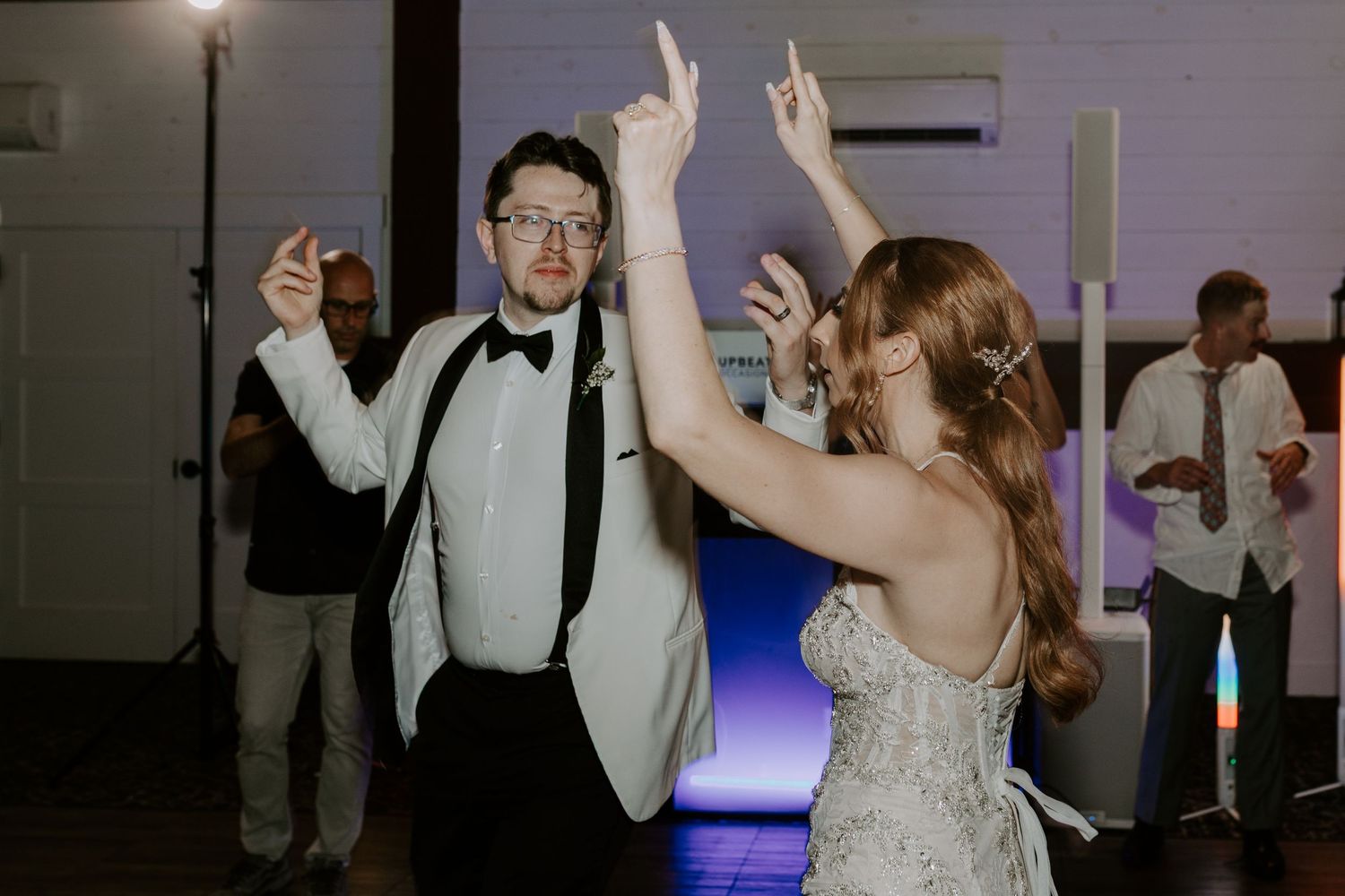 Bride and groom dance with arms raised joyfully on the wedding reception dance floor.