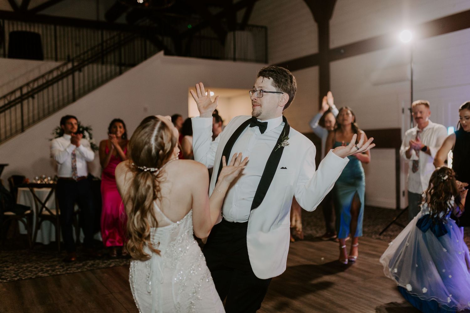 Bride and groom share a lively dance surrounded by cheering guests at their reception.