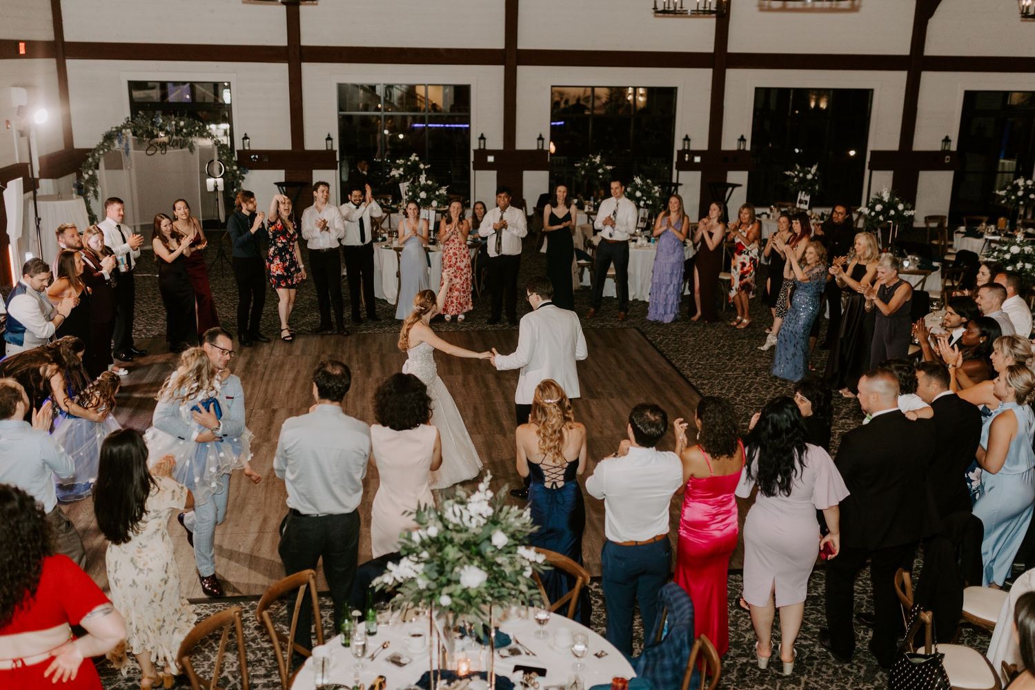 Aerial view of bride and groom dancing in circle with guests at wedding reception.