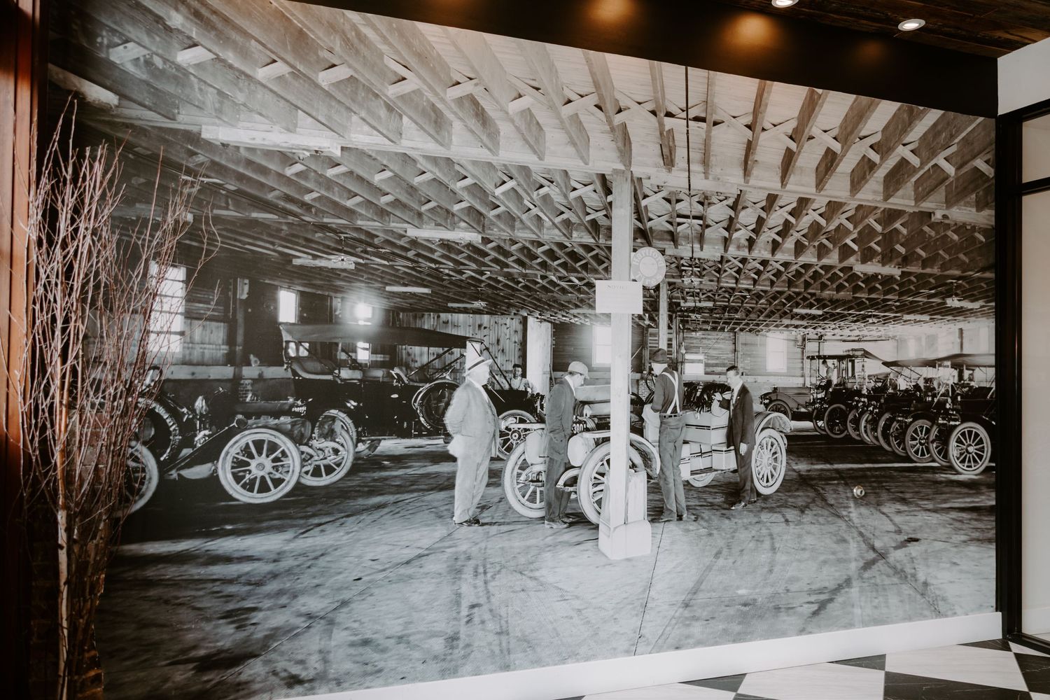 Vintage black and white photo of classic antique automobiles inside a historic carriage house garage.