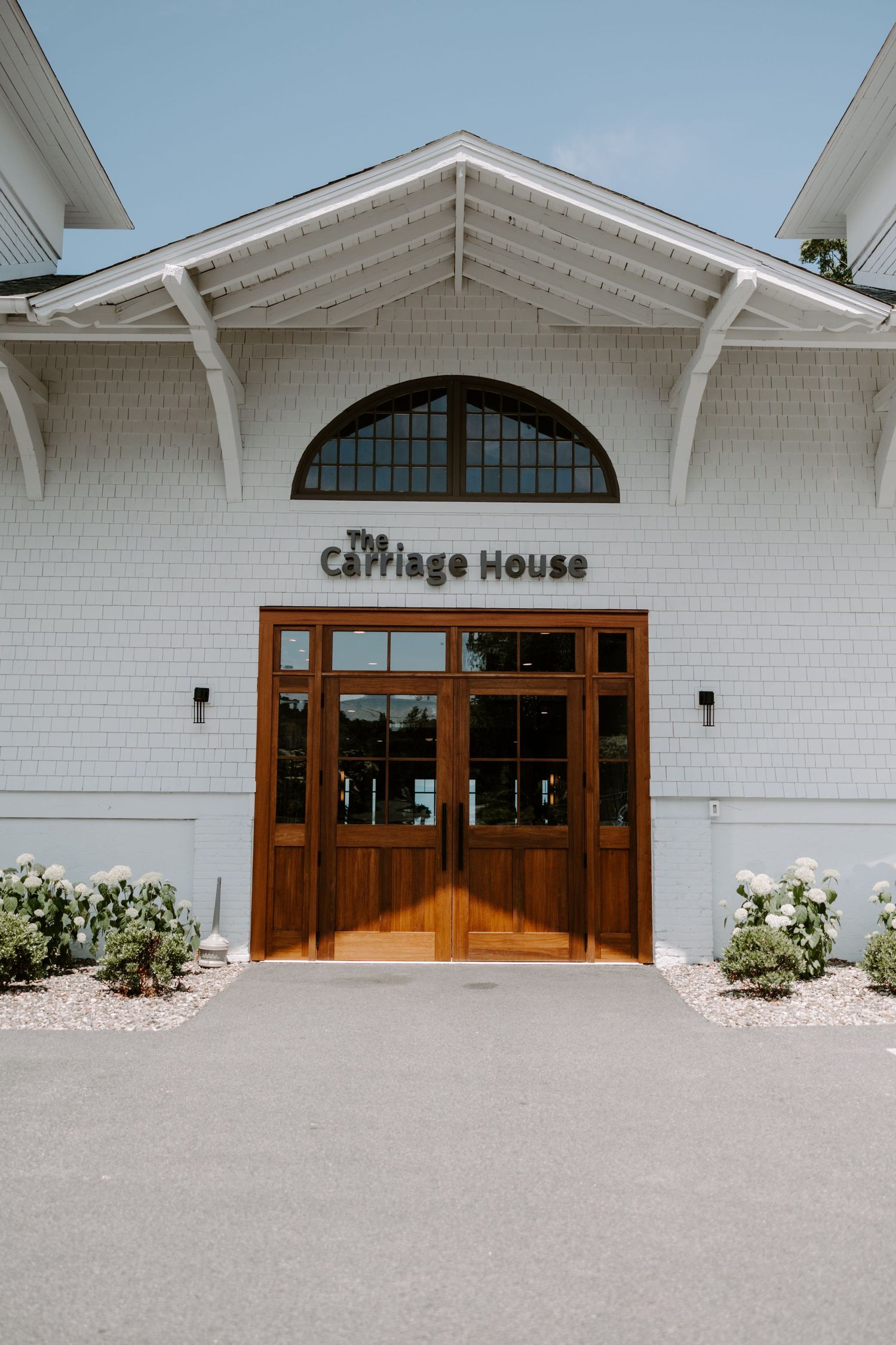 Exterior entrance of The Carriage House venue with white shingle siding and elegant wooden double doors.