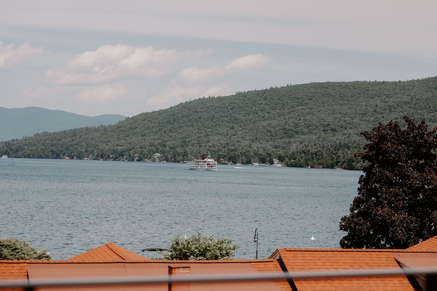 Scenic view of Lake George with a boat on the water and lush green tree-covered mountains in the background.
