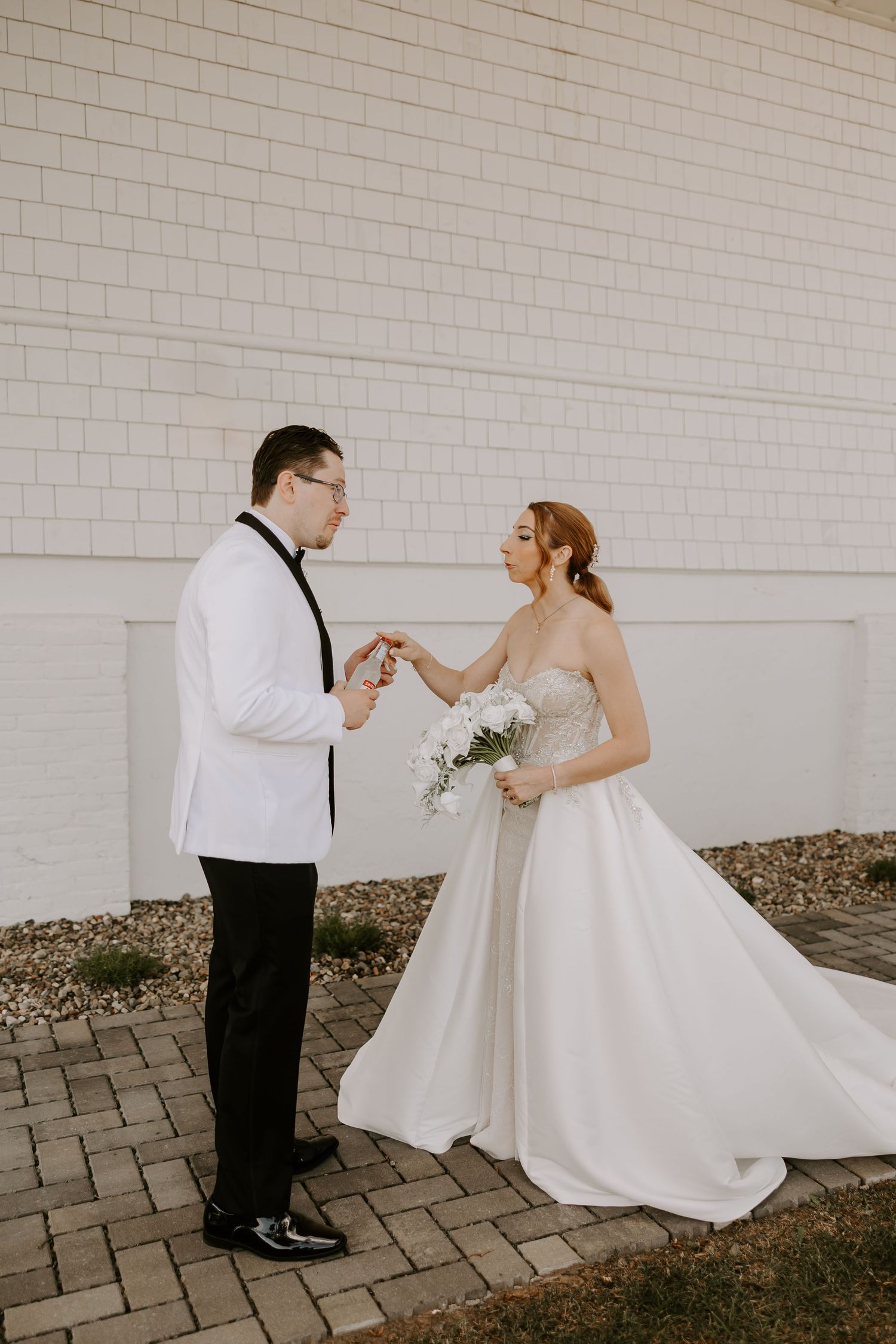 Bride and groom share a tender hand-holding moment during their first look outside a white shingle venue.