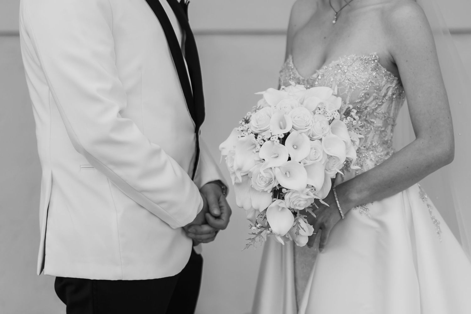 Black and white photo of bride and groom holding hands, bride holding white rose bouquet.