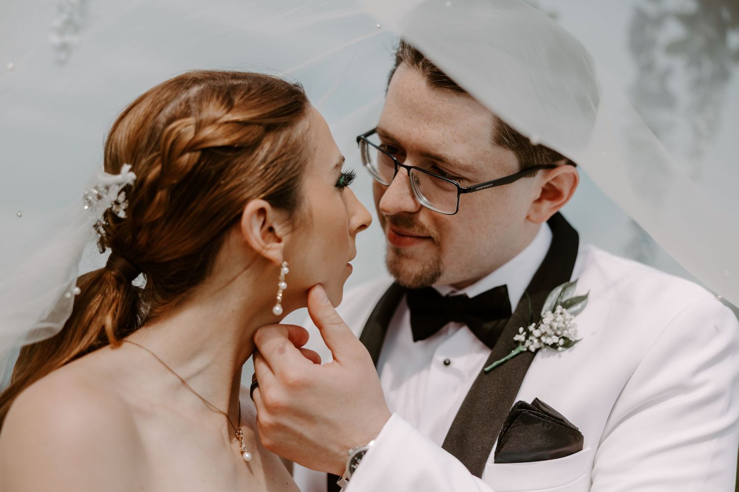 Close-up of bride and groom sharing intimate moment, groom in white tuxedo with bow tie.