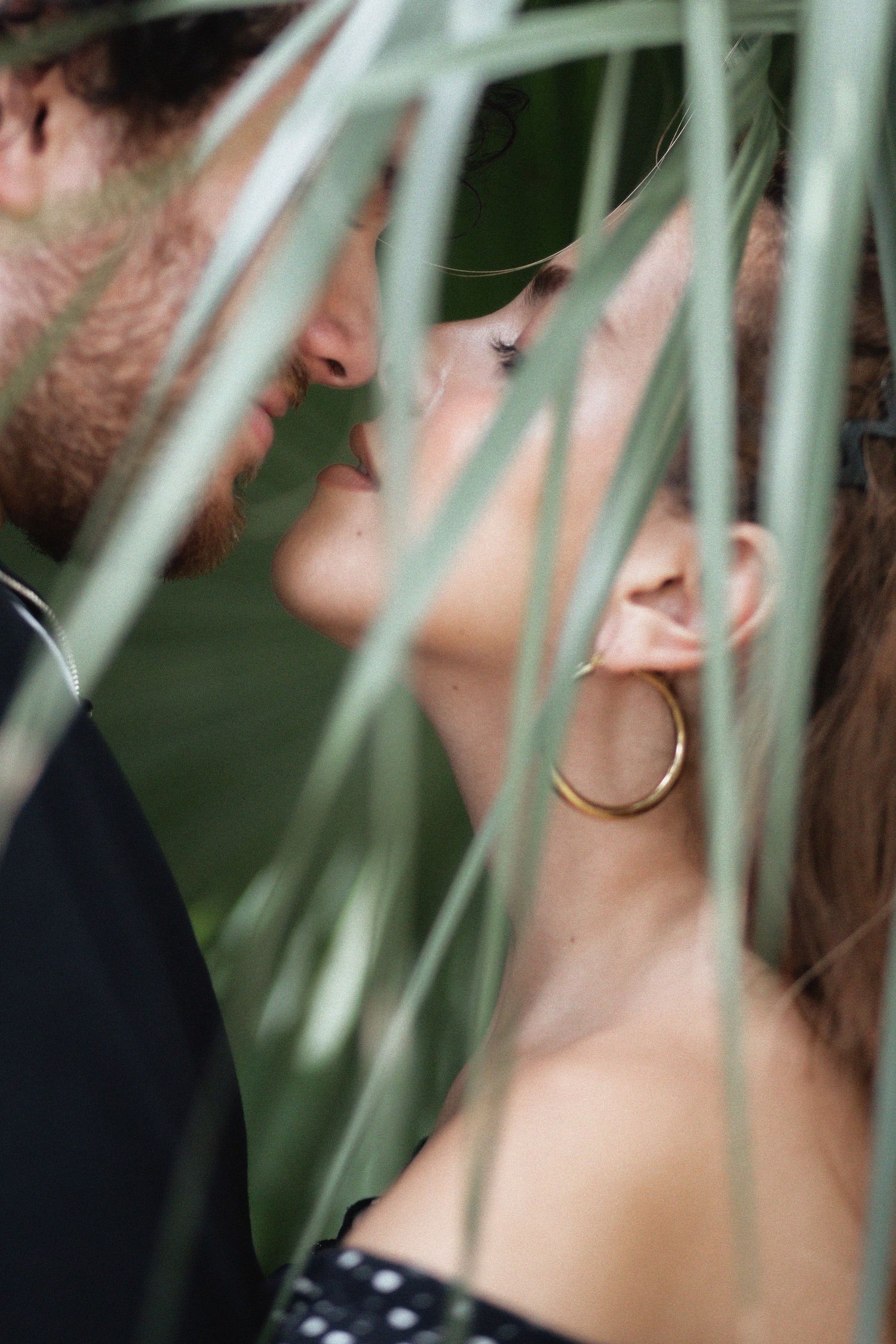 Couple kissing behind tropical palm tree at Kendall Indian Hammocks Park Miami during engagement couples session.