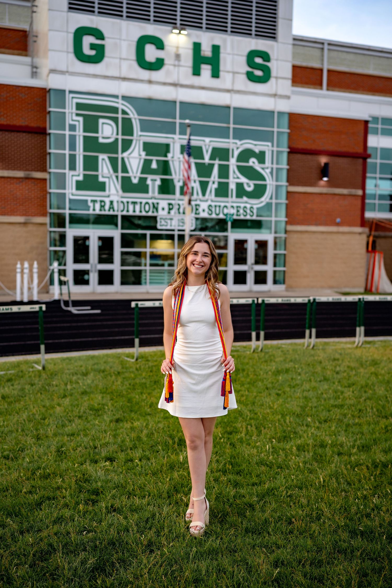 A student stands in front of GCHS school building with green lettering and signage on a sunny day.