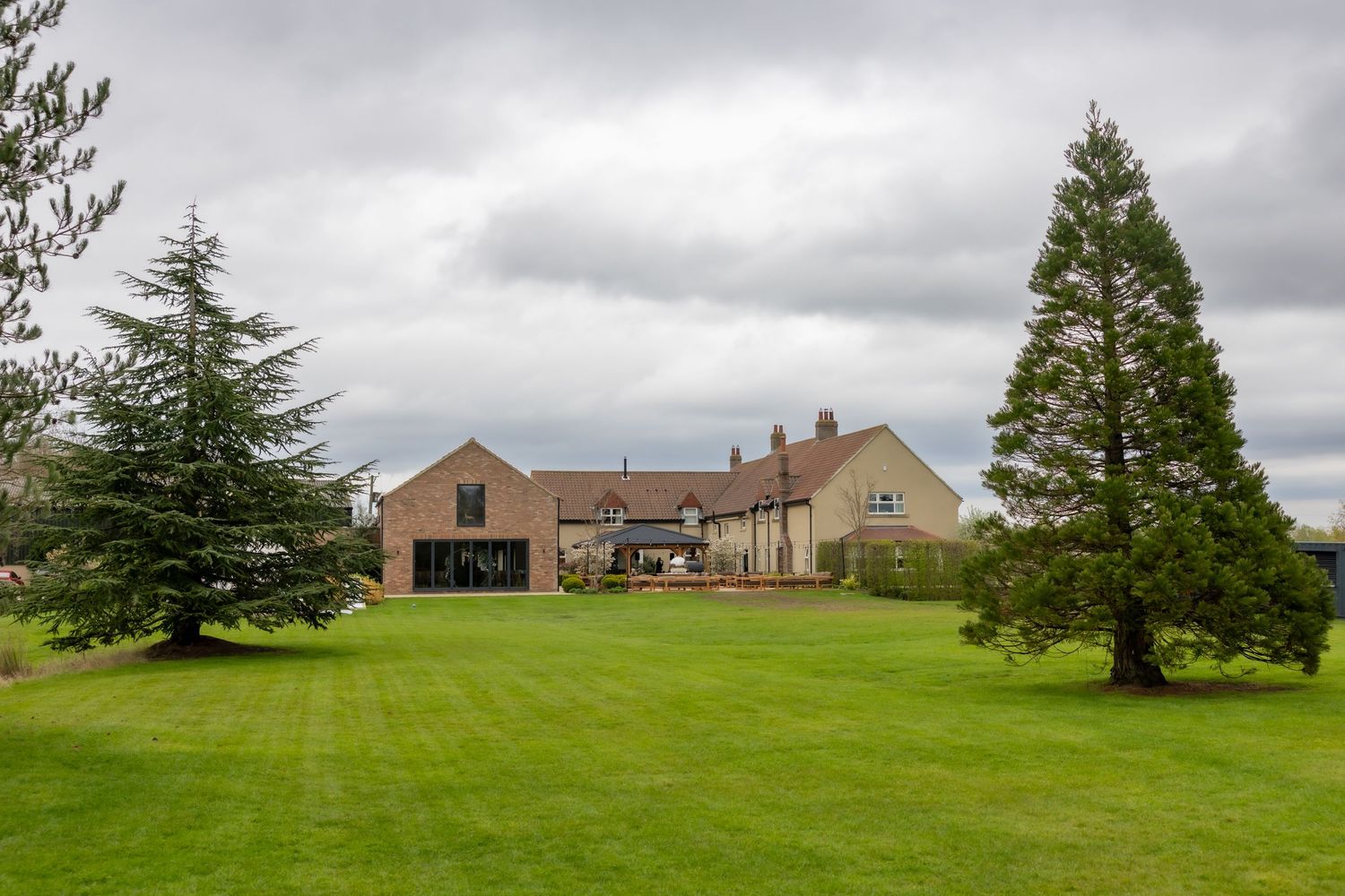 Large country house with expansive green lawn, surrounded by tall evergreen trees under a cloudy sky. Hidden Oak, wedding Casual Captures