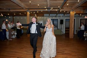 Wedding guests dance together on a rustic wooden dance floor under twinkling string lights at an indoor reception.
