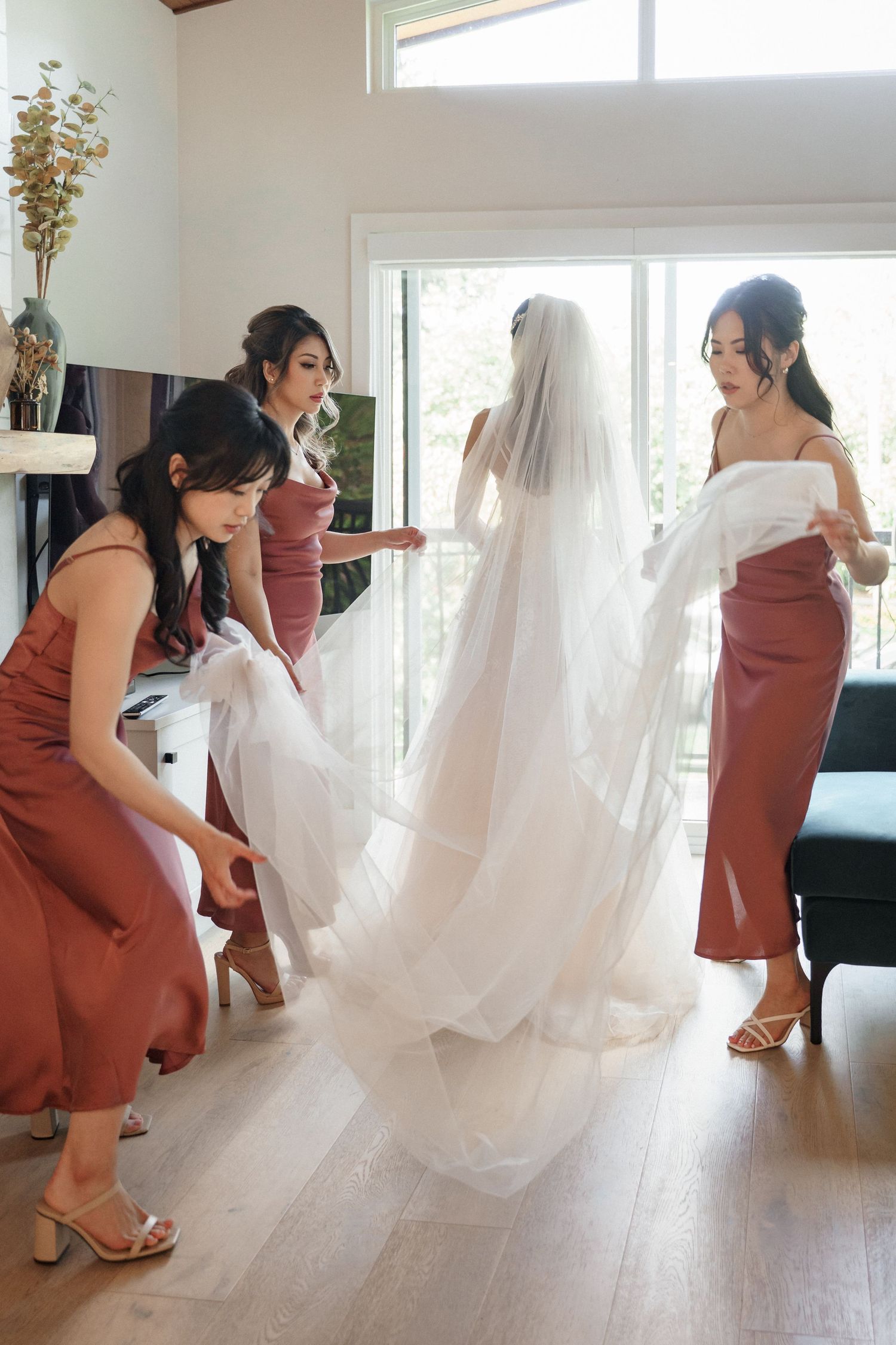 A sequence of photos showing bridesmaids in rust-colored dresses helping adjust a flowing white wedding veil.Queen Elizabeth Park Wedding