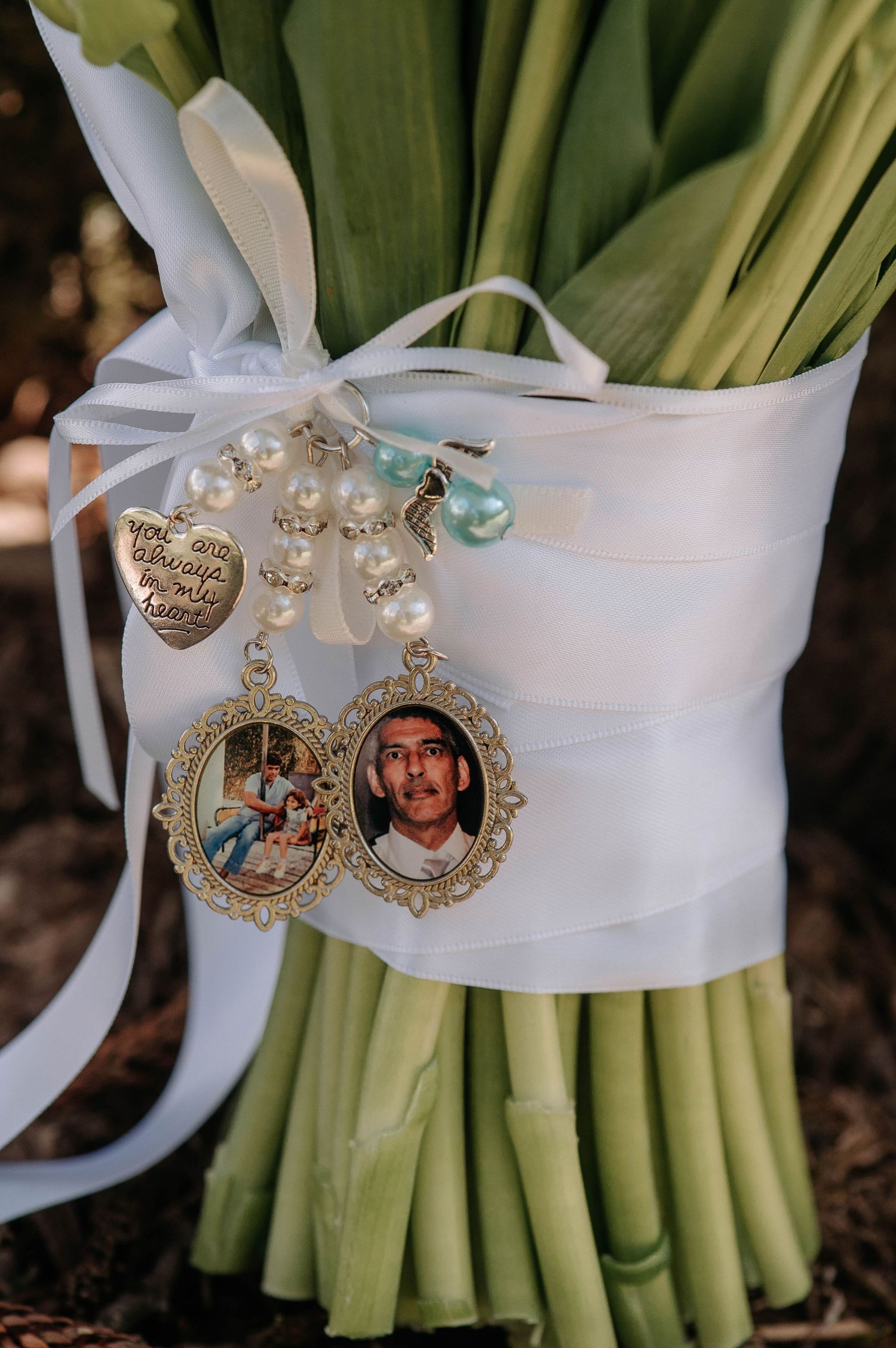Pearl beaded bouquet charm with vintage-style locket medallions tied with white ribbon around green stems.