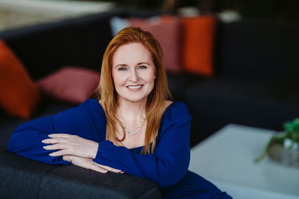 A person in a royal blue sweater reclines comfortably on a dark couch while smiling warmly.