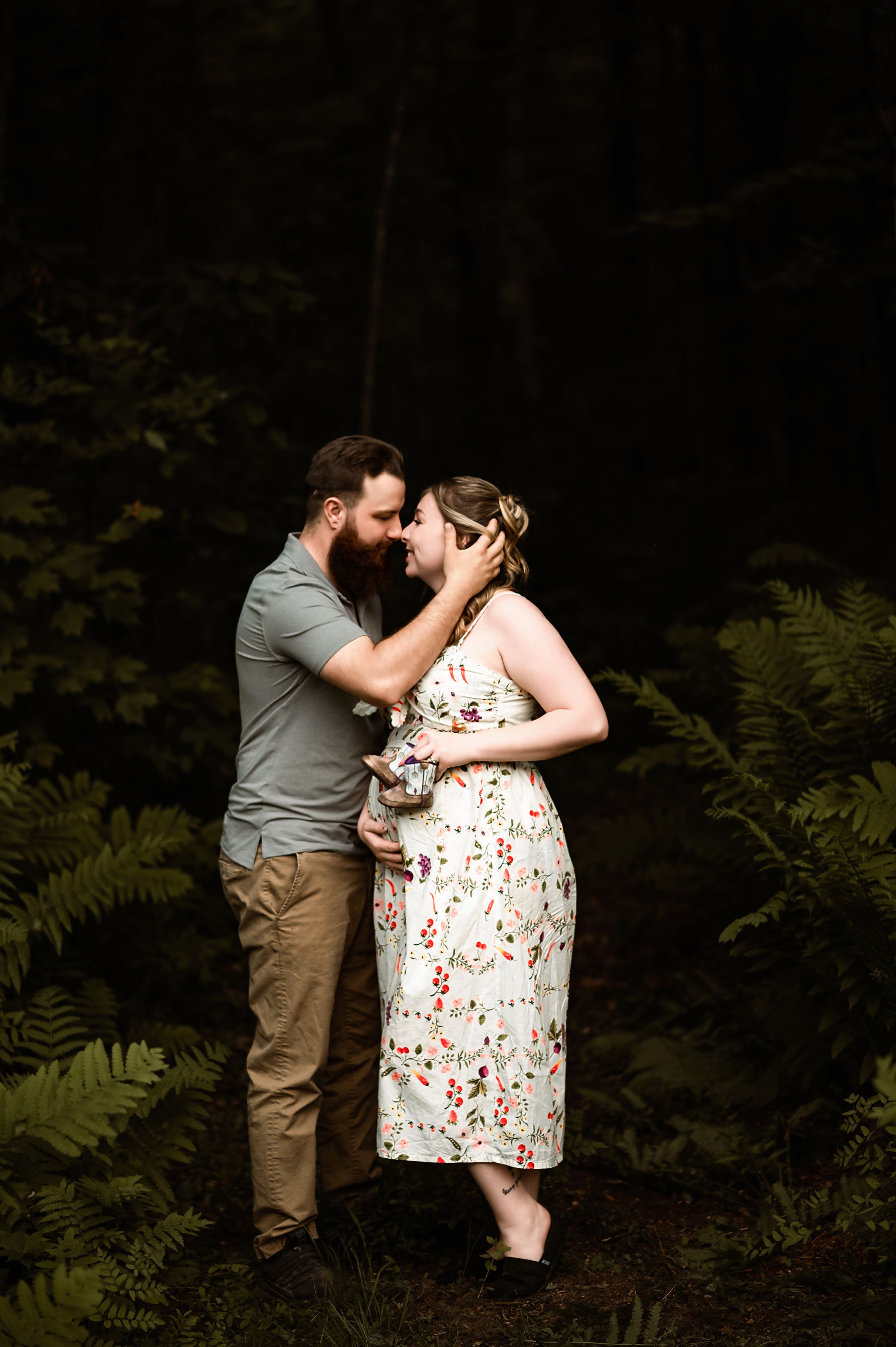 A romantic scene unfolds as a couple embraces in a wooded area with ferns in the background.