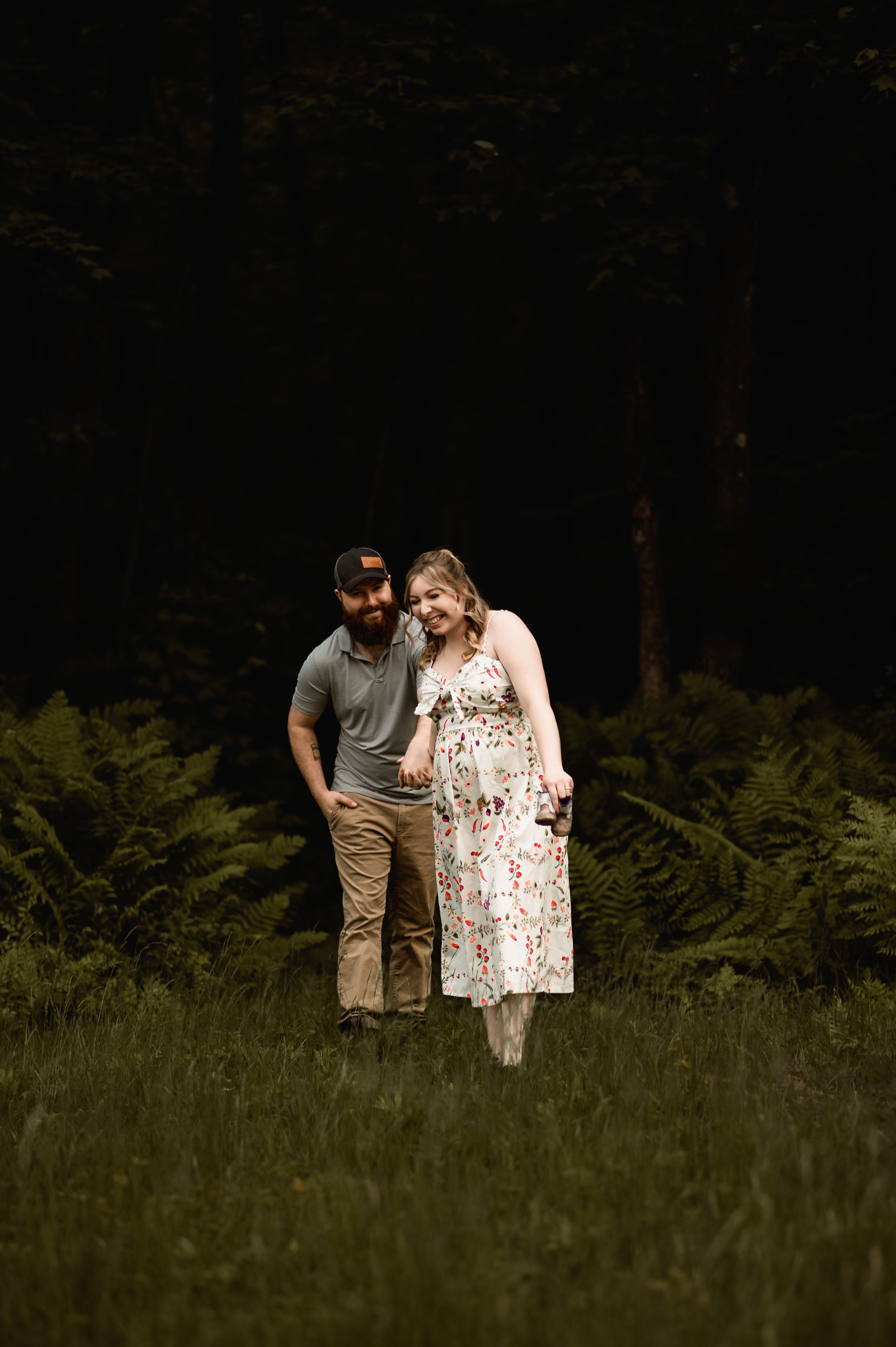 Couple shares intimate moments while standing in tall grass near a forest edge at dusk.