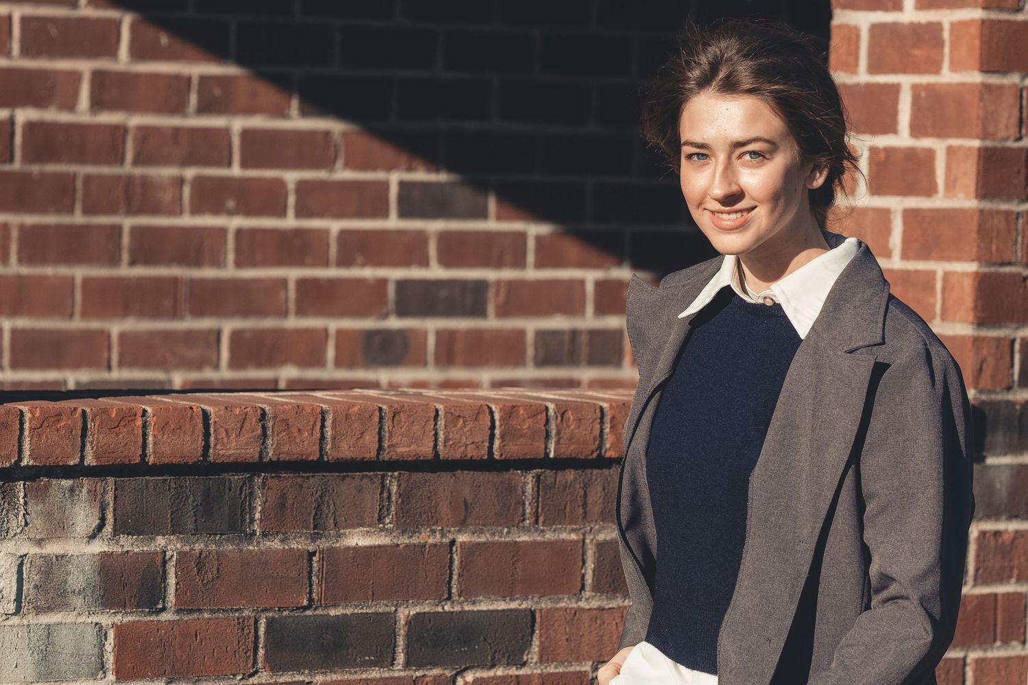 Professional portrait against a brick wall on a sunny day showing warm lighting and classic style.