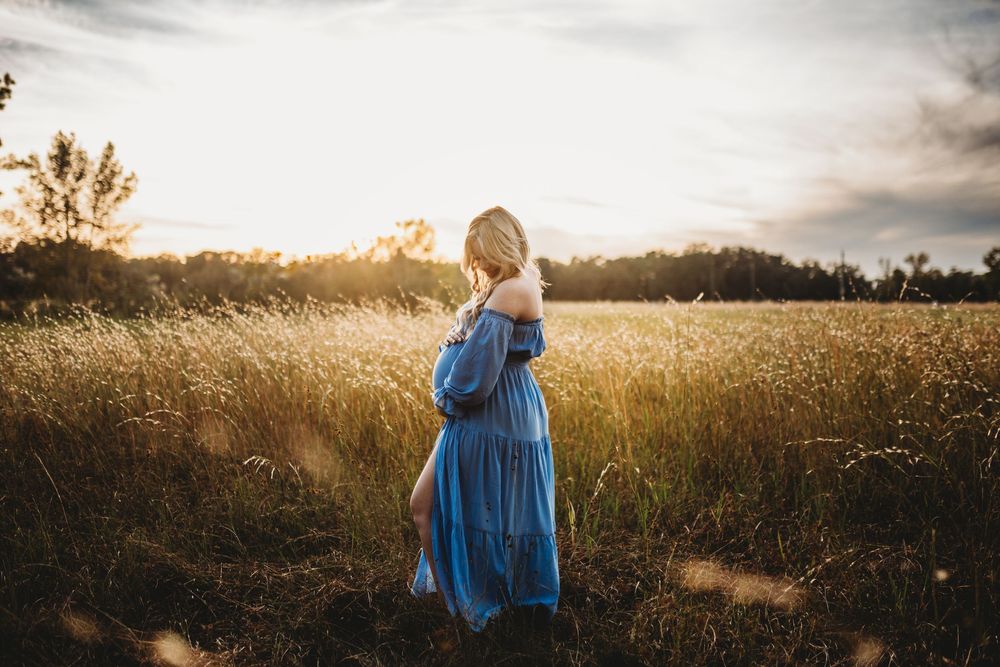 A silhouetted figure in a flowing blue dress stands in a golden wheat field at sunset.
