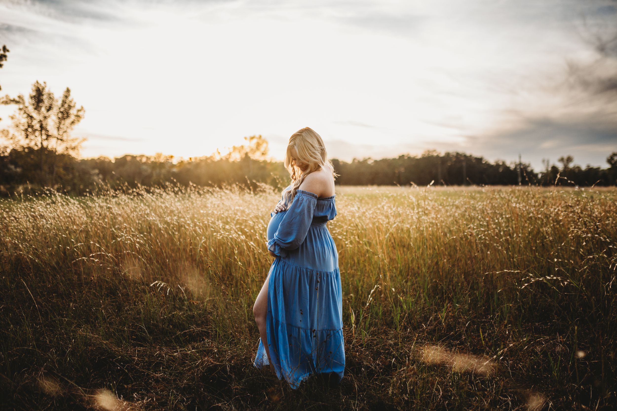 A silhouetted figure in a flowing blue dress stands in a golden wheat field at sunset.