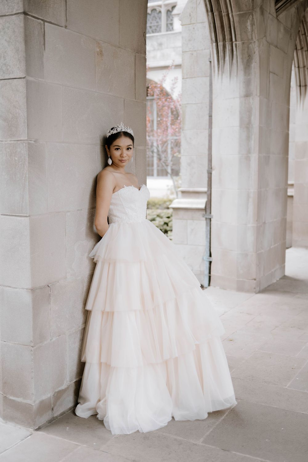 A bride in a stunning layered tulle ballgown poses elegantly in a stone archway with beautiful Gothic architecture.
