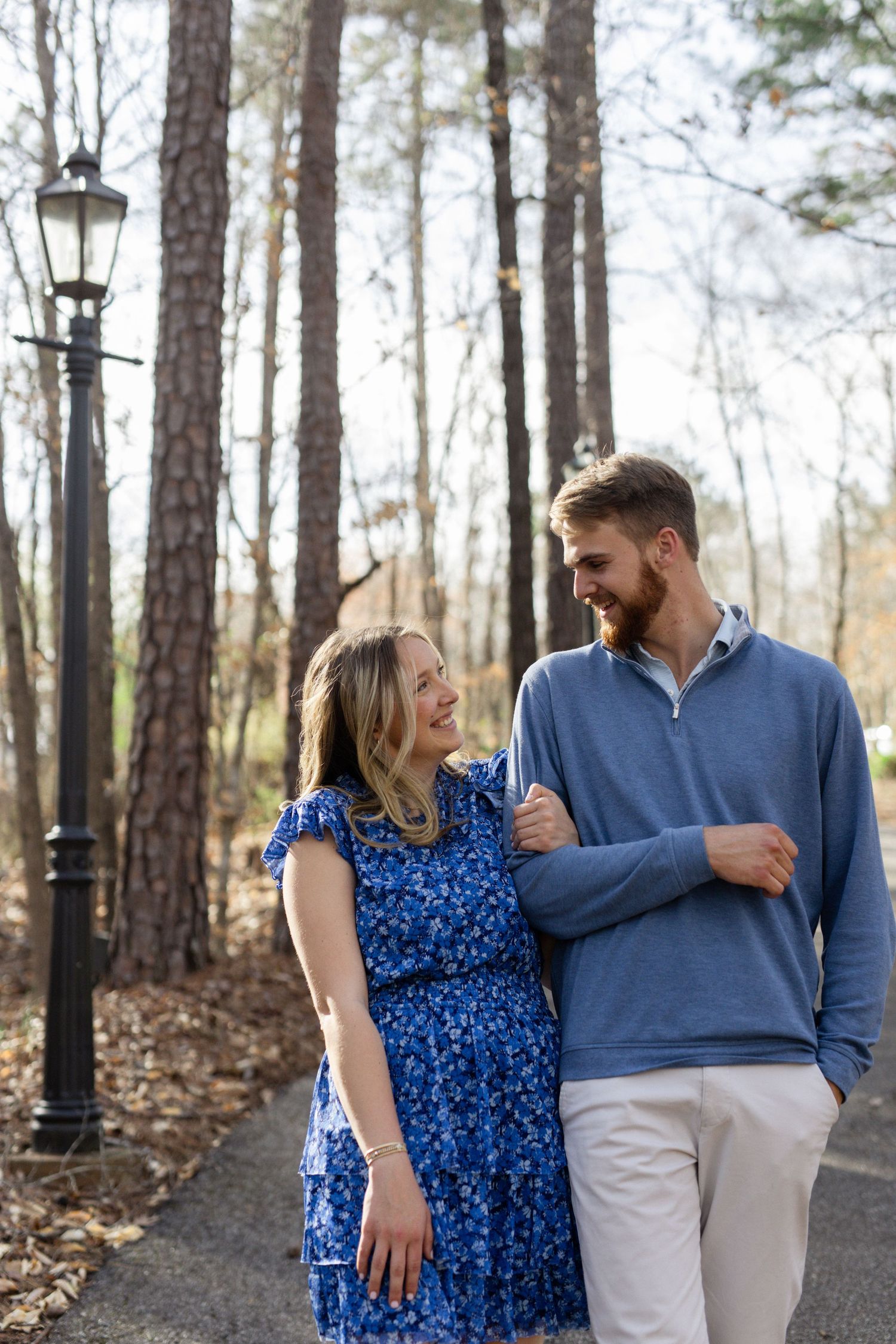 Couple walking and laughing together on path through pine forest wearing coordinated blue outfits.