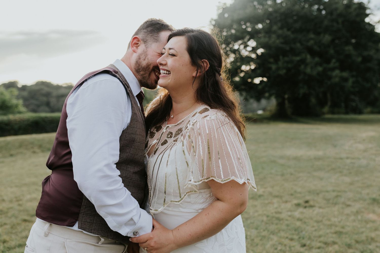 A joyful couple shares a tender moment outdoors in a grassy field during golden hour.
