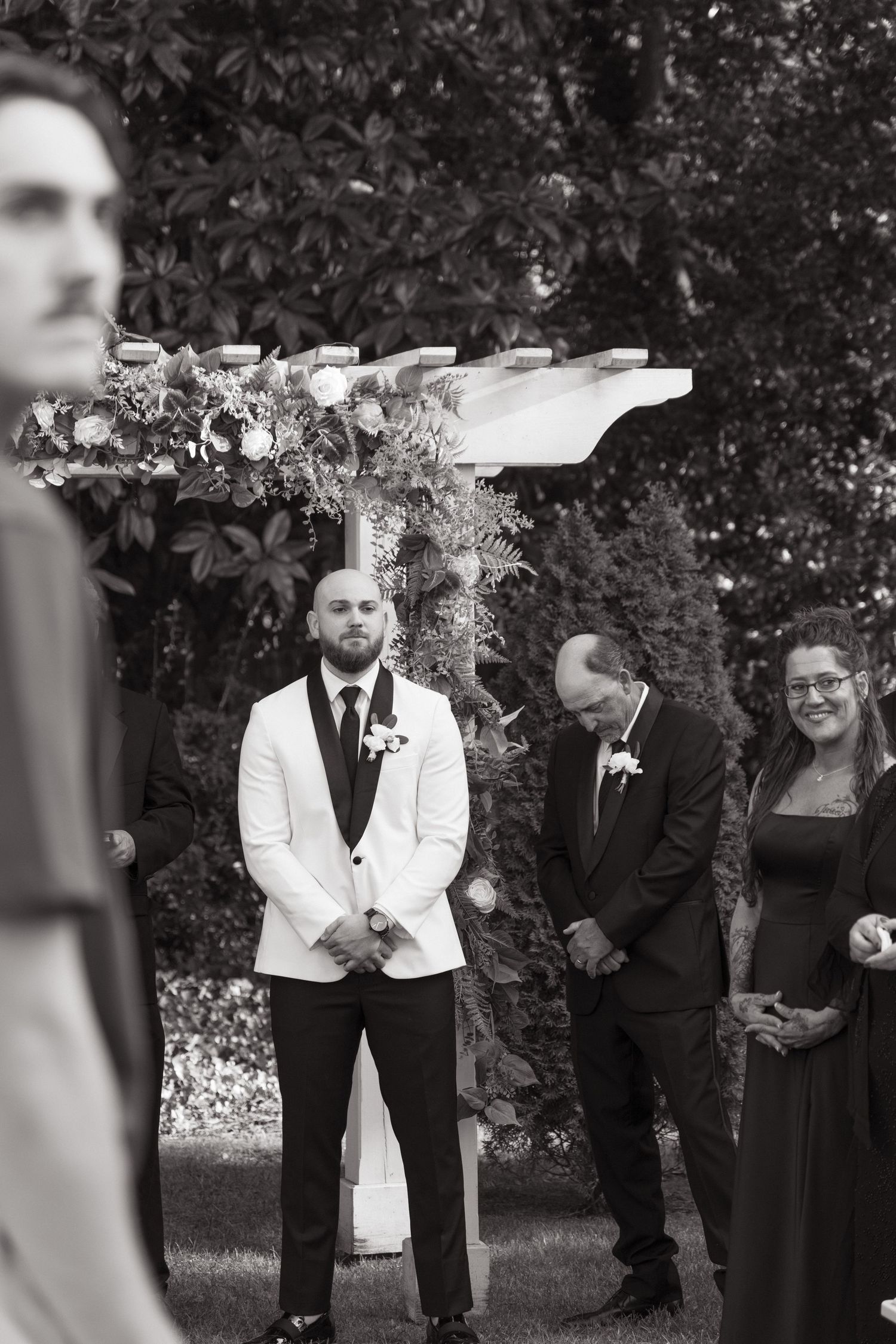 Black and white wedding ceremony photo showing people gathered outdoors in a garden setting.