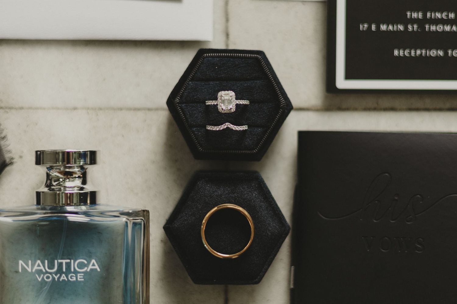 Elegant jewelry display with engagement ring in black hexagonal box next to Nautica perfume bottle and other accessories.