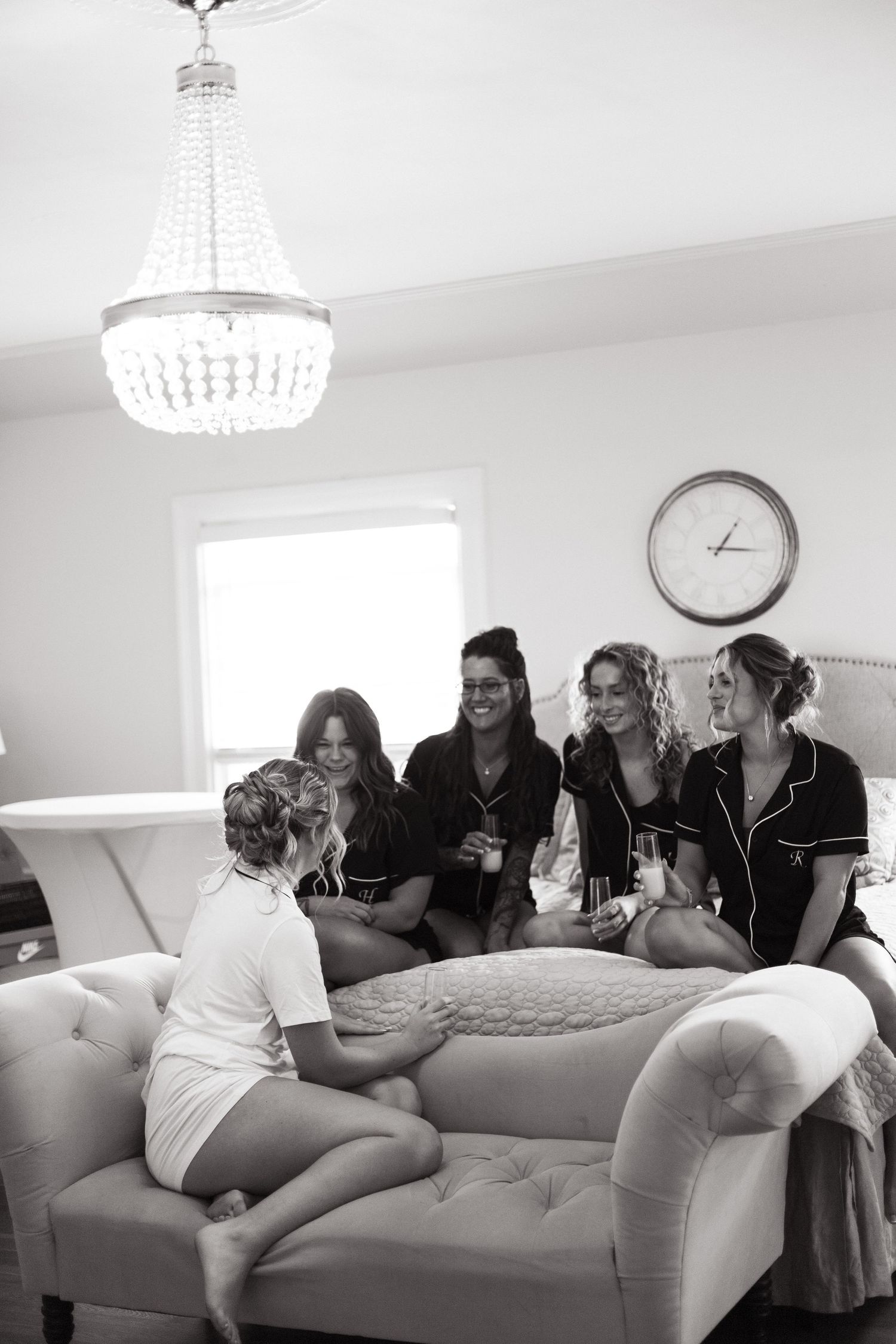 A group gathers on an elegant white couch beneath a crystal chandelier for a social gathering in black and white.