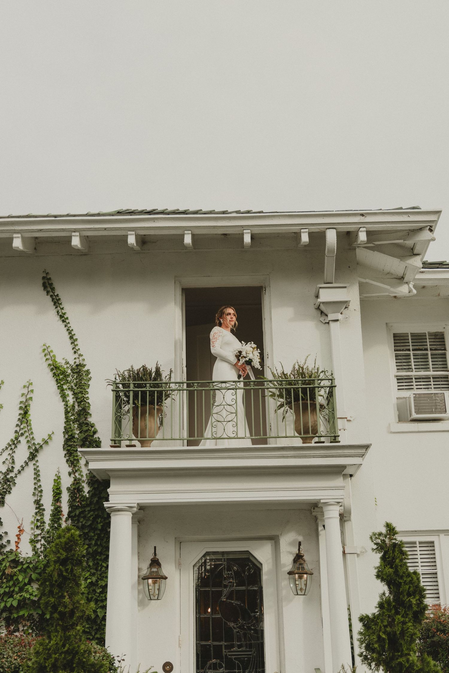 Classic white Mediterranean-style house with ornate balcony railings, twin lanterns, and climbing vines on display.