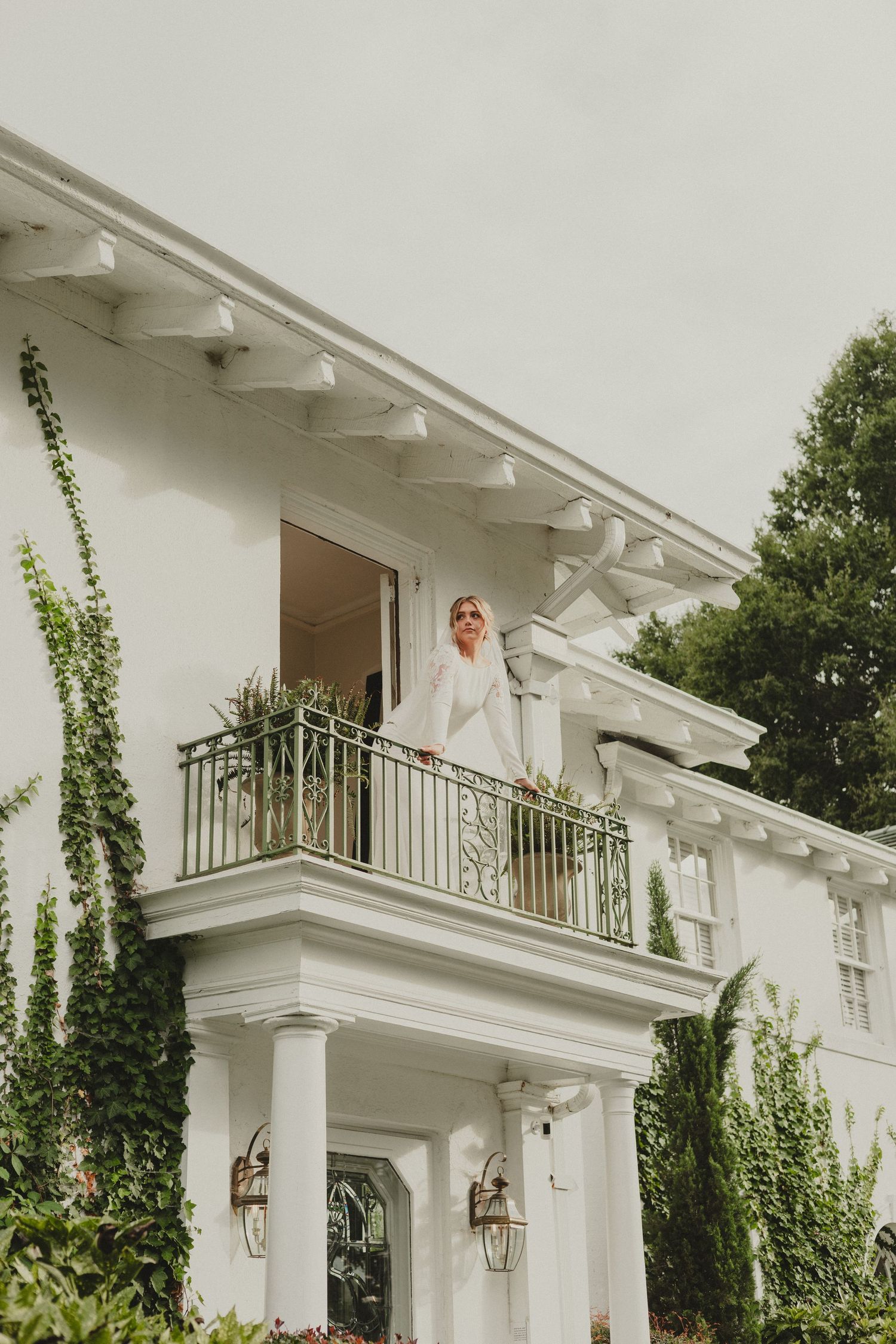 Elegant white mansion with climbing ivy and decorative balcony featuring classic southern architecture and gas lanterns.