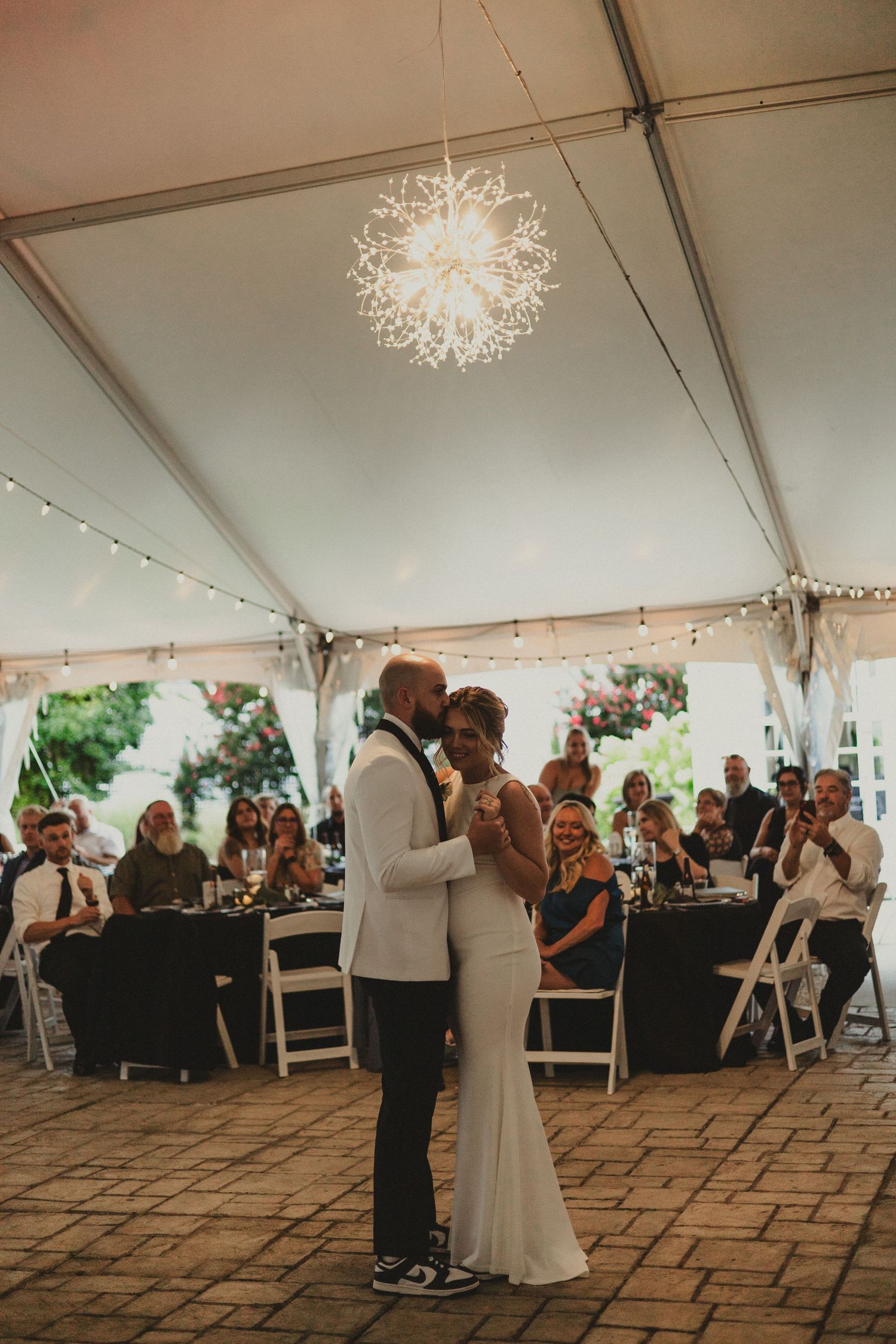 Couple sharing their first dance under a decorative chandelier in an elegant white tent reception space.