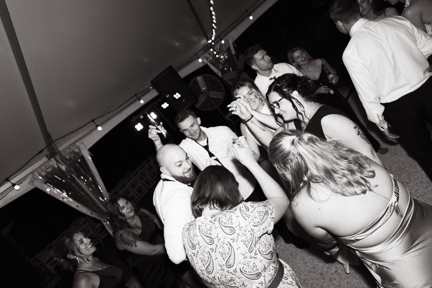 A crowd of people dance together at a dark nightclub or party venue captured in black and white.