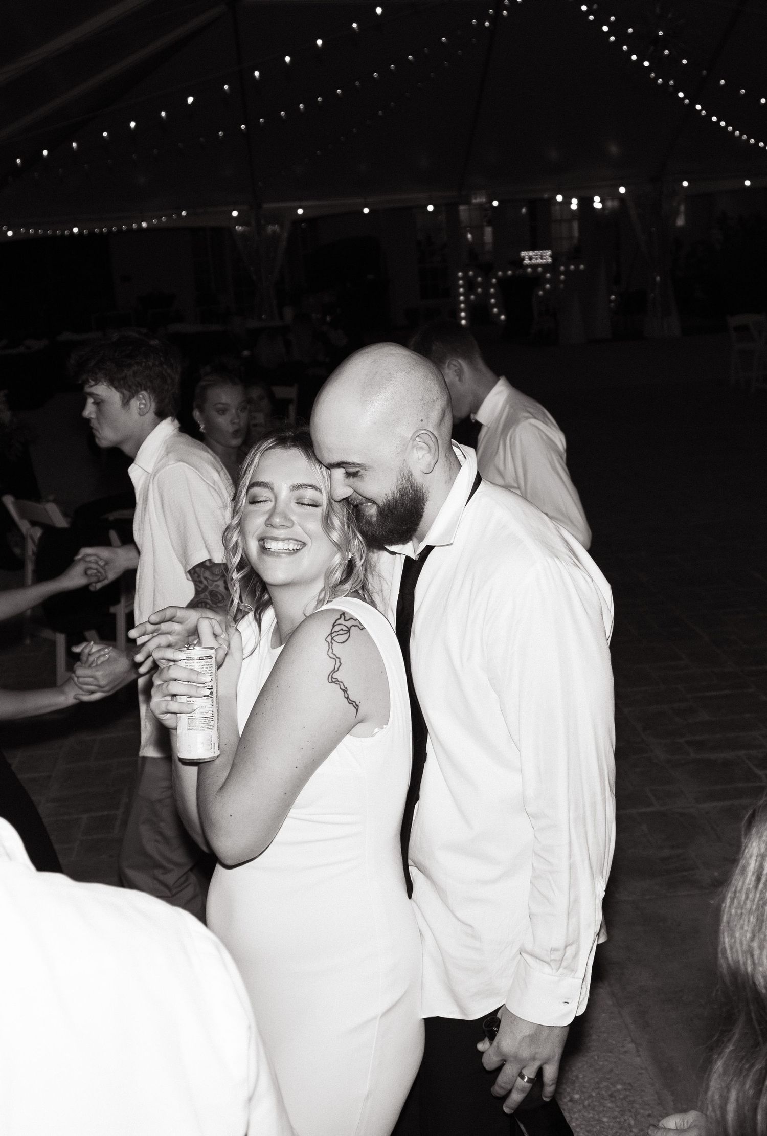 Black and white photo of a couple dancing together at a party venue decorated with string lights.