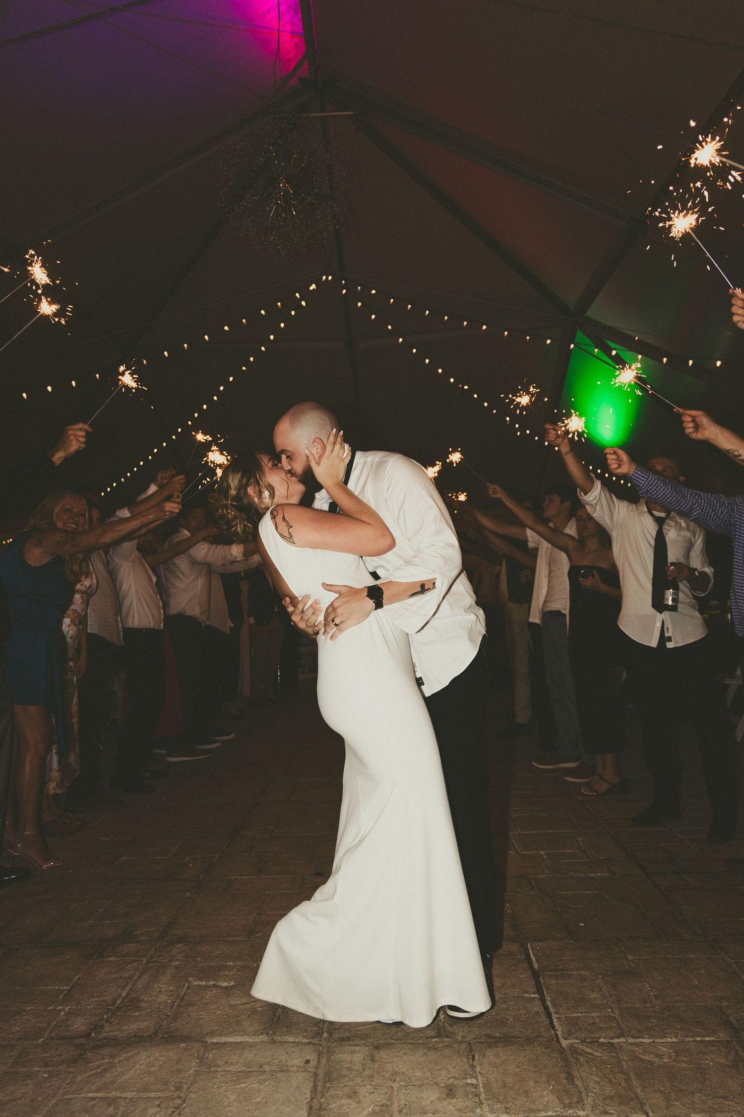 A couple sharing a romantic dance under string lights at their wedding reception in a tented venue.