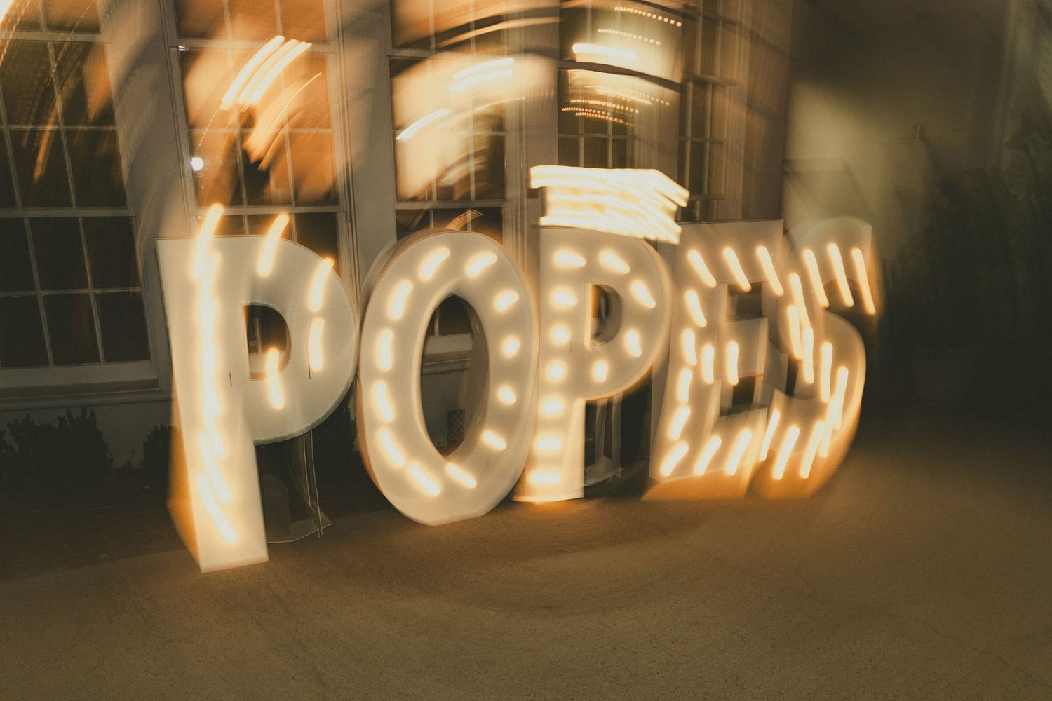 A blurry marquee sign with illuminated letters spelling out 'POPS' glowing warmly in a dim interior setting.