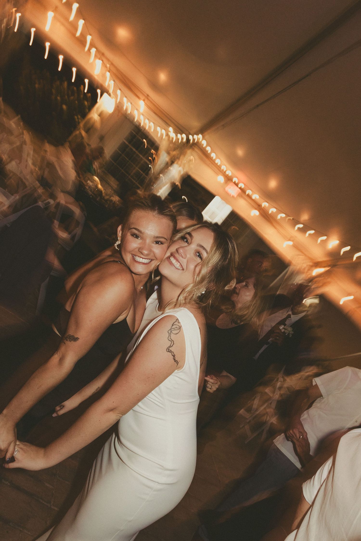 Guests dancing together at a wedding reception under warm string lights and decorative lighting.